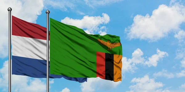 Niederlande und Sambia schwenken gemeinsam die Flagge im Wind gegen den wolkenverhangenen blauen Himmel. Diplomatie-Konzept, internationale Beziehungen. — Stockfoto
