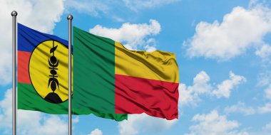 Yeni Kaledonya ve Benin bayrağı birlikte beyaz bulutlu mavi gökyüzüne karşı rüzgarda sallayarak. Diplomasi kavramı, uluslararası ilişkiler.