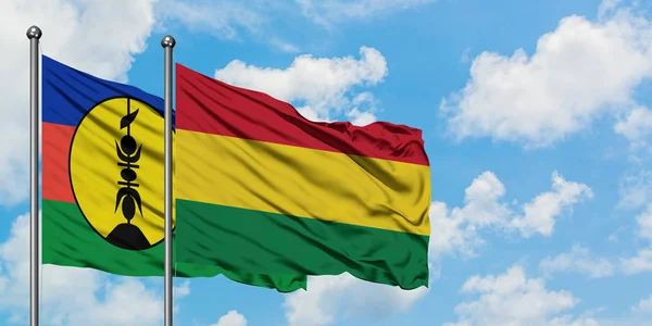 Bandera de Nueva Caledonia y Bolivia ondeando en el viento contra el cielo azul nublado blanco juntos. Concepto diplomático, relaciones internacionales . — Foto de Stock