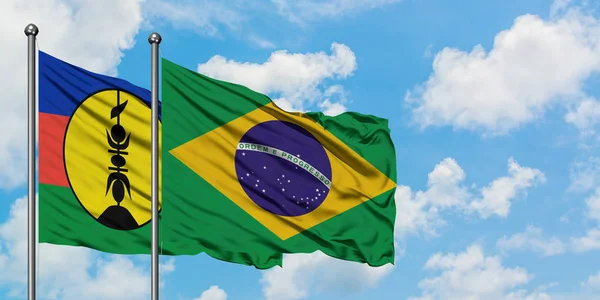 Bandera de Nueva Caledonia y Brasil ondeando en el viento contra el cielo azul nublado blanco juntos. Concepto diplomático, relaciones internacionales . — Foto de Stock