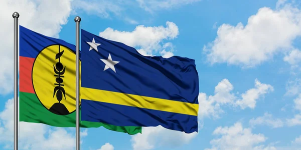 Bandera de Nueva Caledonia y Curazao ondeando en el viento contra el cielo azul nublado blanco juntos. Concepto diplomático, relaciones internacionales . — Foto de Stock