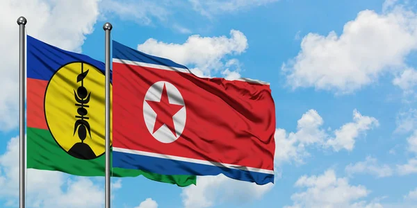 Új-Kaledónia és Észak-Korea zászló integetett a szél ellen, fehér felhős kék eget együtt. Diplomáciai koncepció, nemzetközi kapcsolatok. — Stock Fotó