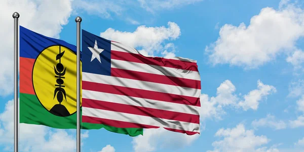 一緒に白い曇った青い空に対して風に手を振るニューカレドニアとリベリアの旗。外交概念、国際関係. — ストック写真