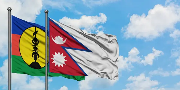 Bandera de Nueva Caledonia y Nepal ondeando en el viento contra el cielo azul nublado blanco juntos. Concepto diplomático, relaciones internacionales . — Foto de Stock