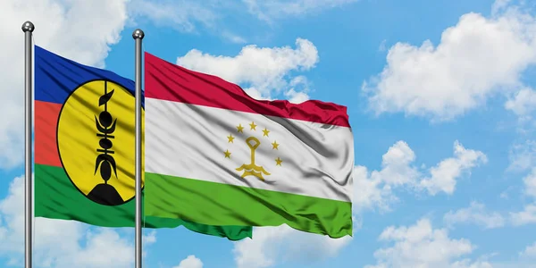 Bandera de Nueva Caledonia y Tayikistán ondeando en el viento contra el cielo azul nublado blanco juntos. Concepto diplomático, relaciones internacionales . — Foto de Stock