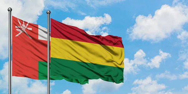 Bandera de Omán y Bolivia ondeando en el viento contra el cielo azul nublado blanco juntos. Concepto diplomático, relaciones internacionales . — Foto de Stock