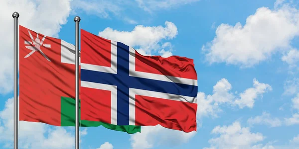 Bandera de Omán y Bouvet Islands ondeando en el viento contra el cielo azul nublado blanco juntos. Concepto diplomático, relaciones internacionales . — Foto de Stock