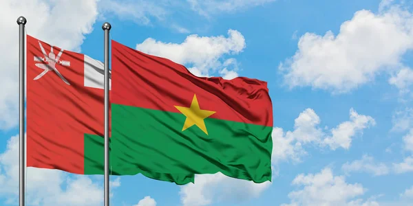 Omán y Burkina Faso ondeando en el viento contra el cielo azul nublado blanco juntos. Concepto diplomático, relaciones internacionales . — Foto de Stock