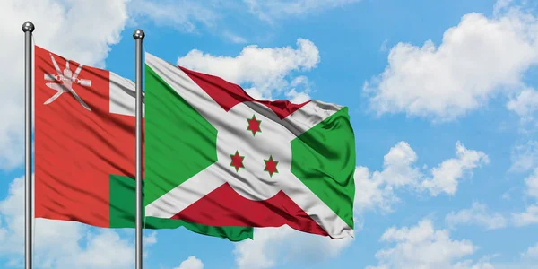 Bandera de Omán y Burundi ondeando en el viento contra el cielo azul nublado blanco juntos. Concepto diplomático, relaciones internacionales . — Foto de Stock