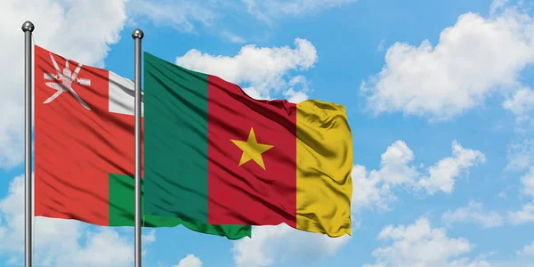 Bandera de Omán y Camerún ondeando en el viento contra el cielo azul nublado blanco juntos. Concepto diplomático, relaciones internacionales . — Foto de Stock