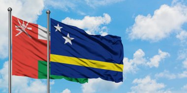 Umman ve Curacao bayrağı birlikte beyaz bulutlu mavi gökyüzüne karşı rüzgarda sallayarak. Diplomasi kavramı, uluslararası ilişkiler.