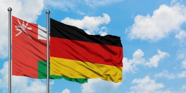 Umman ve Almanya bayrağı birlikte beyaz bulutlu mavi gökyüzüne karşı rüzgarda sallayarak. Diplomasi kavramı, uluslararası ilişkiler.