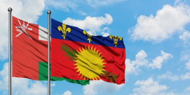 Umman ve Guadeloupe bayrağı birlikte beyaz bulutlu mavi gökyüzüne karşı rüzgarda sallayarak. Diplomasi kavramı, uluslararası ilişkiler.
