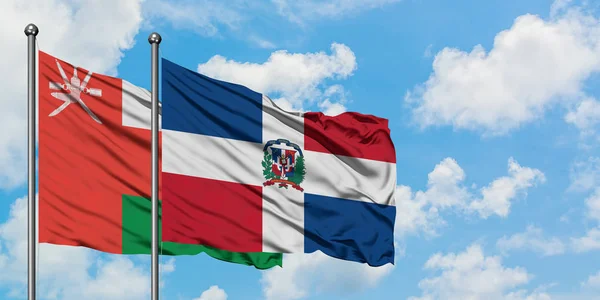 オマーンとドミニカ共和国の旗は、一緒に白い曇り青い空に対して風に手を振る。外交概念、国際関係. — ストック写真