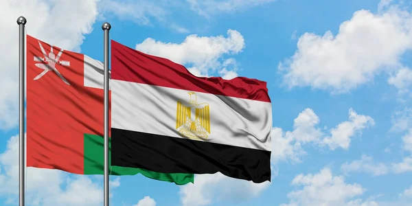 Omán y Egipto bandera ondeando en el viento contra el blanco cielo azul nublado juntos. Concepto diplomático, relaciones internacionales . — Foto de Stock