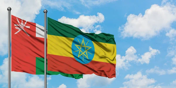 Omán a Etiopie vlaje ve větru proti bíle zatažené modré obloze. Diplomacie, mezinárodní vztahy. — Stock fotografie