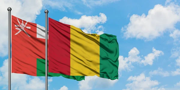 Bandera de Omán y Guinea ondeando en el viento contra el cielo azul nublado blanco juntos. Concepto diplomático, relaciones internacionales . — Foto de Stock