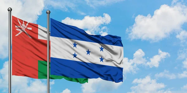 Bandera de Omán y Honduras ondeando en el viento contra el cielo azul nublado blanco juntos. Concepto diplomático, relaciones internacionales . — Foto de Stock