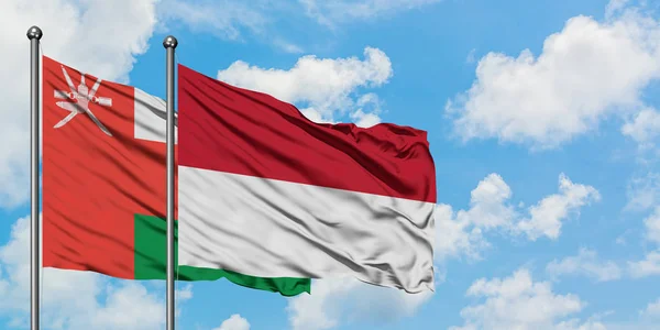 Bandera de Omán e Indonesia ondeando en el viento contra el cielo azul nublado blanco juntos. Concepto diplomático, relaciones internacionales . — Foto de Stock