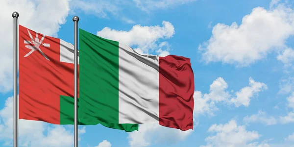 Bandera de Omán e Italia ondeando en el viento contra el cielo azul nublado blanco juntos. Concepto diplomático, relaciones internacionales . — Foto de Stock