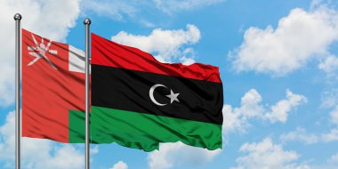 Umman ve Libya bayrağı birlikte beyaz bulutlu mavi gökyüzüne karşı rüzgarda sallayarak. Diplomasi kavramı, uluslararası ilişkiler.