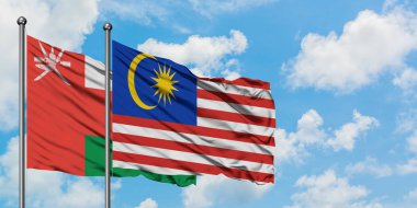 Umman ve Malezya bayrağı birlikte beyaz bulutlu mavi gökyüzüne karşı rüzgarda sallayarak. Diplomasi kavramı, uluslararası ilişkiler.