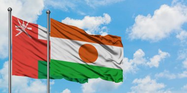 Umman ve Nijer bayrağı birlikte beyaz bulutlu mavi gökyüzüne karşı rüzgarda sallayarak. Diplomasi kavramı, uluslararası ilişkiler.