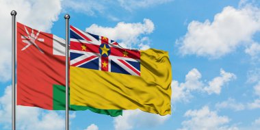 Umman ve Niue bayrağı birlikte beyaz bulutlu mavi gökyüzüne karşı rüzgarda sallayarak. Diplomasi kavramı, uluslararası ilişkiler.