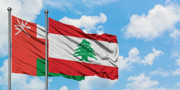 Bandera de Omán y Líbano ondeando en el viento contra el cielo azul nublado blanco juntos. Concepto diplomático, relaciones internacionales . — Foto de Stock