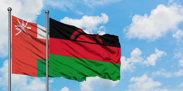 Bandera de Omán y Malawi ondeando en el viento contra el cielo azul nublado blanco juntos. Concepto diplomático, relaciones internacionales . — Foto de Stock