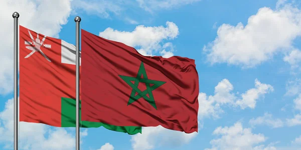 Bandera de Omán y Marruecos ondeando en el viento contra el cielo azul nublado blanco juntos. Concepto diplomático, relaciones internacionales . — Foto de Stock