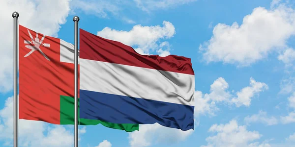 stock image Oman and Netherlands flag waving in the wind against white cloudy blue sky together. Diplomacy concept, international relations.