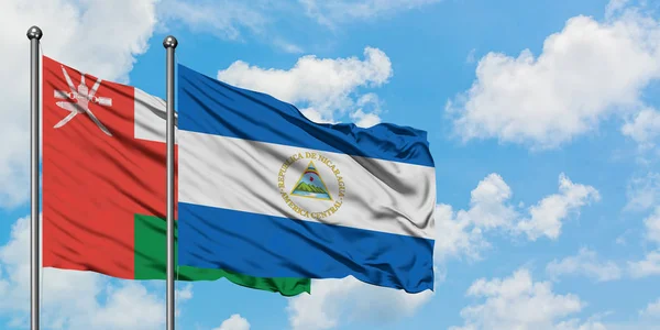 Bandera de Omán y Nicaragua ondeando en el viento contra el cielo azul nublado blanco juntos. Concepto diplomático, relaciones internacionales . — Foto de Stock