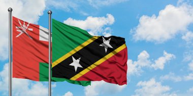 Umman ve Saint Kitts ve Nevis bayrağı birlikte beyaz bulutlu mavi gökyüzüne karşı rüzgarda sallayarak. Diplomasi kavramı, uluslararası ilişkiler.