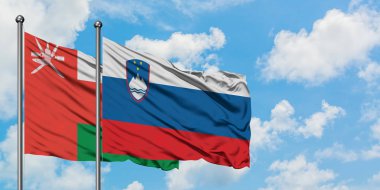 Umman ve Slovenya bayrağı birlikte beyaz bulutlu mavi gökyüzüne karşı rüzgarda sallayarak. Diplomasi kavramı, uluslararası ilişkiler.