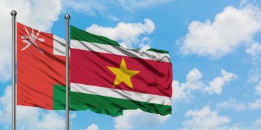 Umman ve Surinam bayrağı birlikte beyaz bulutlu mavi gökyüzüne karşı rüzgarsal sallayarak. Diplomasi kavramı, uluslararası ilişkiler.