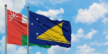 Umman ve Tokelau bayrağı birlikte beyaz bulutlu mavi gökyüzüne karşı rüzgarda sallayarak. Diplomasi kavramı, uluslararası ilişkiler.