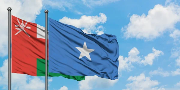 Bandera de Omán y Somalia ondeando en el viento contra el cielo azul nublado blanco juntos. Concepto diplomático, relaciones internacionales . — Foto de Stock