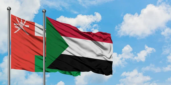 Bandeira de Omã e Sudão agitando no vento contra o céu azul nublado branco juntos. Conceito de diplomacia, relações internacionais . — Fotografia de Stock