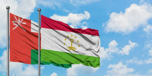 Omán y Tayikistán ondean en el viento contra el cielo azul nublado blanco juntos. Concepto diplomático, relaciones internacionales . — Foto de Stock
