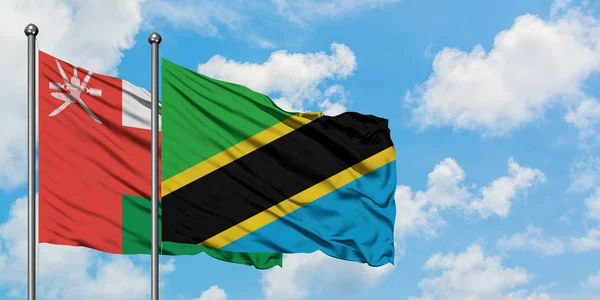 Bandera de Omán y Tanzania ondeando en el viento contra el cielo azul nublado blanco juntos. Concepto diplomático, relaciones internacionales . —  Fotos de Stock