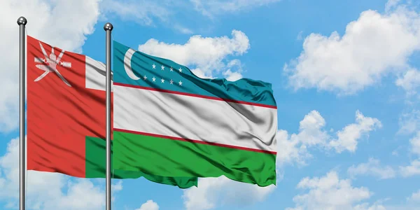 Omán y Uzbekistán bandera ondeando en el viento contra el cielo azul nublado blanco juntos. Concepto diplomático, relaciones internacionales . — Foto de Stock