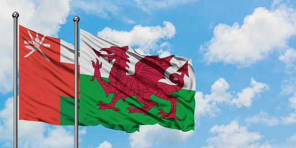 Bandeira de Omã e Gales agitando no vento contra o céu azul nublado branco juntos. Conceito de diplomacia, relações internacionais . — Fotografia de Stock