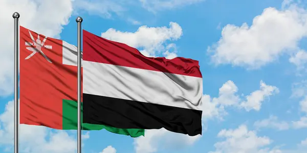 Bandera de Omán y Yemen ondeando en el viento contra el cielo azul nublado blanco juntos. Concepto diplomático, relaciones internacionales . — Foto de Stock