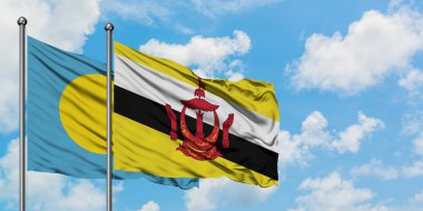 Palau ve Brunei bayrağı birlikte beyaz bulutlu mavi gökyüzüne karşı rüzgarda sallayarak. Diplomasi kavramı, uluslararası ilişkiler.