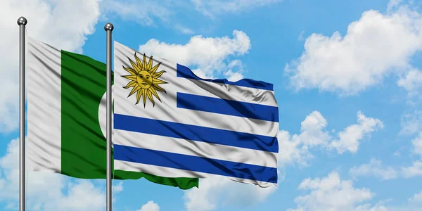 Pakistan e Uruguay sventolano bandiera nel vento contro bianco cielo blu nuvoloso insieme. Concetto di diplomazia, relazioni internazionali . — Foto Stock