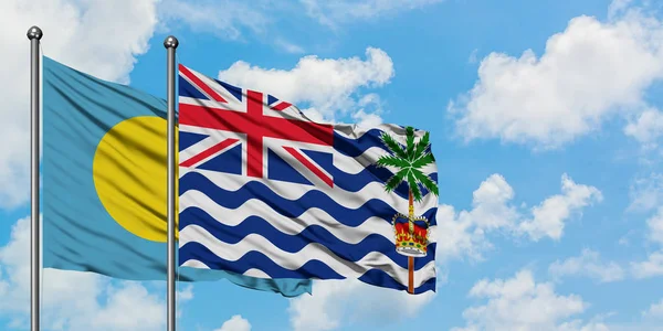 Bandera de Palaos y del Territorio Británico del Océano Índico ondeando en el viento contra el cielo azul nublado blanco juntos. Concepto diplomático, relaciones internacionales . — Foto de Stock