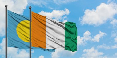 Palau ve Fildişi Sahili bayrağı birlikte beyaz bulutlu mavi gökyüzüne karşı rüzgarda sallayarak. Diplomasi kavramı, uluslararası ilişkiler.