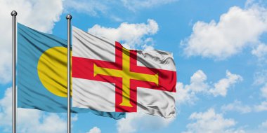Palau ve Guernsey bayrağı birlikte beyaz bulutlu mavi gökyüzüne karşı rüzgarda sallayarak. Diplomasi kavramı, uluslararası ilişkiler.