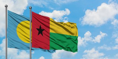 Palau ve Gine Bissau bayrağı birlikte beyaz bulutlu mavi gökyüzüne karşı rüzgarda sallayarak. Diplomasi kavramı, uluslararası ilişkiler.